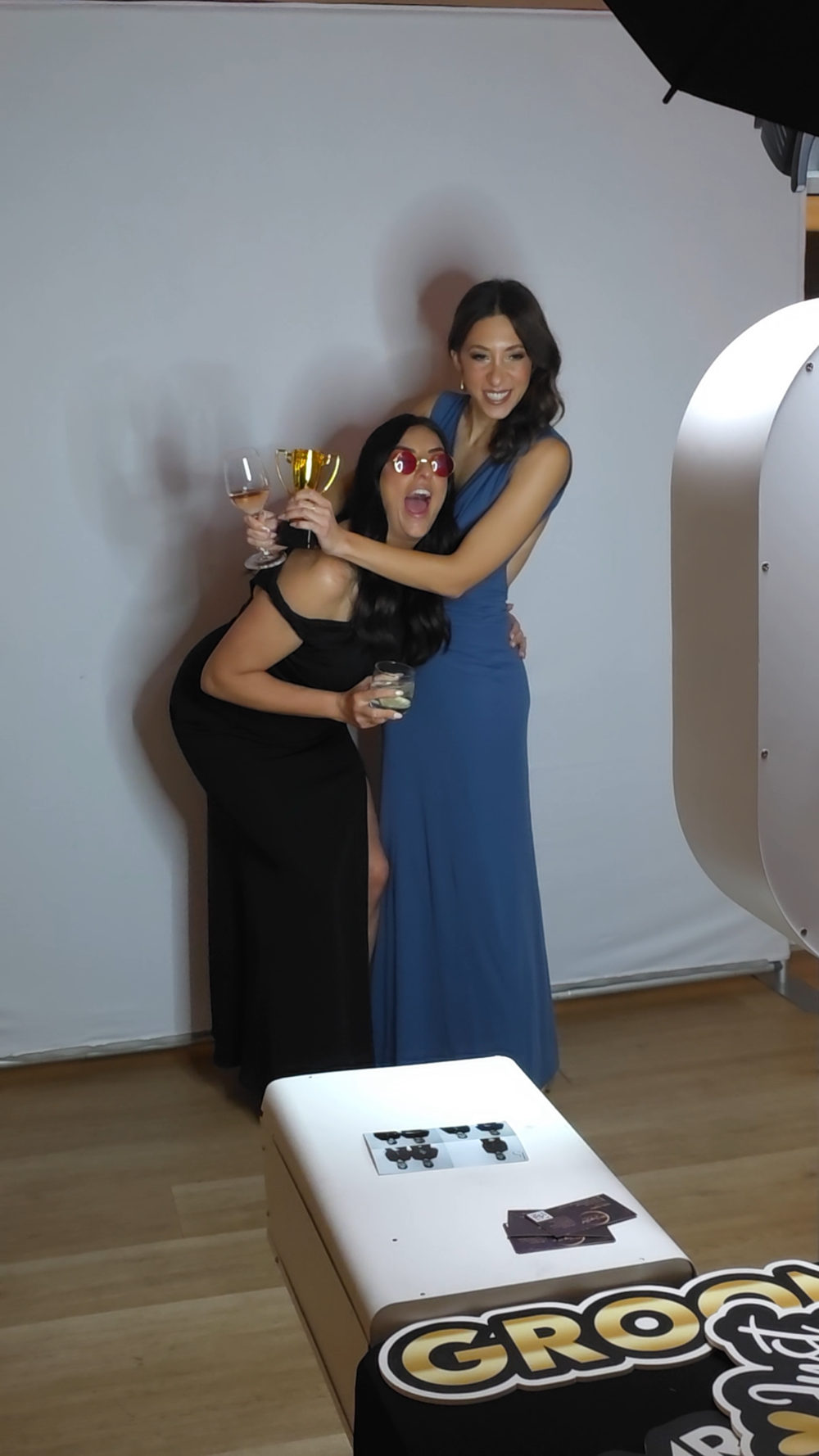 Two guests in formal dresses posing with props in front of the Luxe photo booth backdrop at an Adelaide event